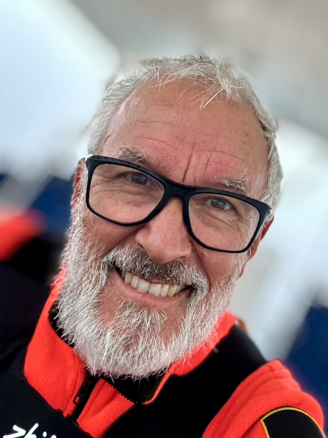 Bruce Maunsell smiling aboard in a red sailing jacket